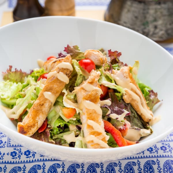 Grilled chicken salad with mixed greens, cherry tomatoes, and creamy dressing in a white bowl.