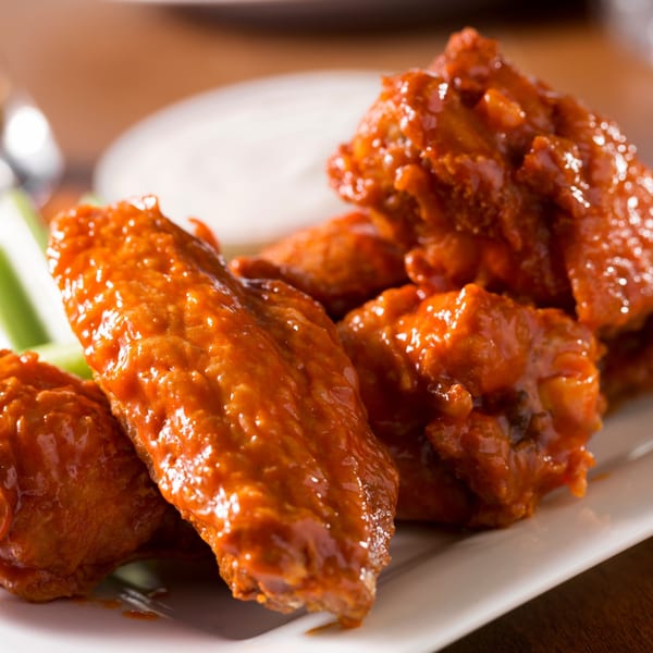 Spicy buffalo chicken wings with celery sticks and ranch dressing on a white plate.
