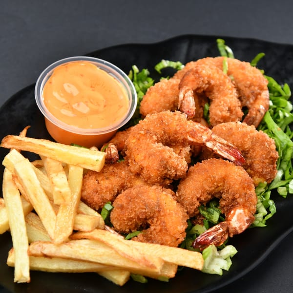 Crispy fried shrimp and golden french fries with a side of orange dipping sauce on a black plate.